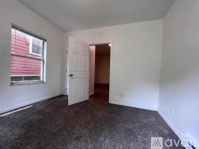 A room with a carpeted floor, a white door, and a window with red blinds.