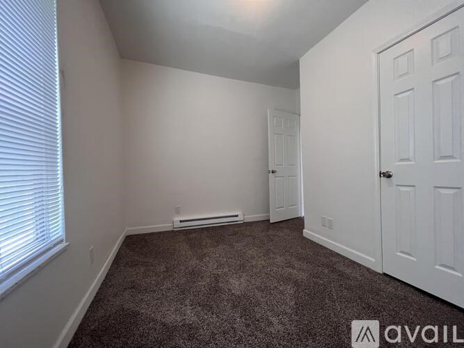 A room with a carpeted floor, a window with blinds, and a white door.