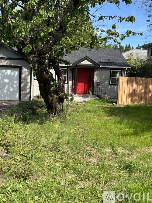 A house with a red door is surrounded by a grassy area and a tree.