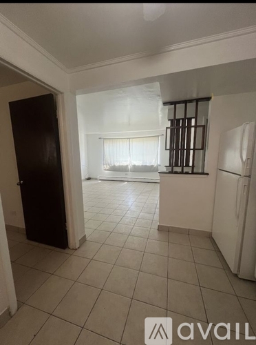 A kitchen area with a refrigerator and a window with curtains.