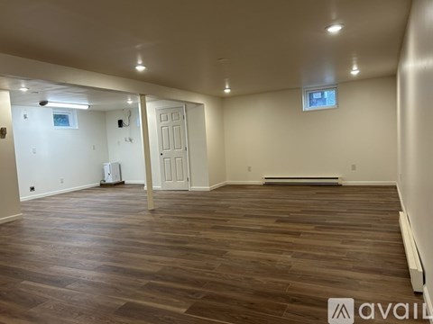 A spacious room with wooden flooring and white walls.