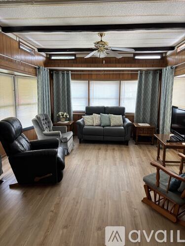 A living room with a black leather chair, a grey couch, a wooden rocking chair, and a television.