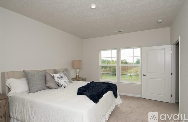A bedroom with a large bed, a nightstand with a lamp, and a window with a view of the outside.