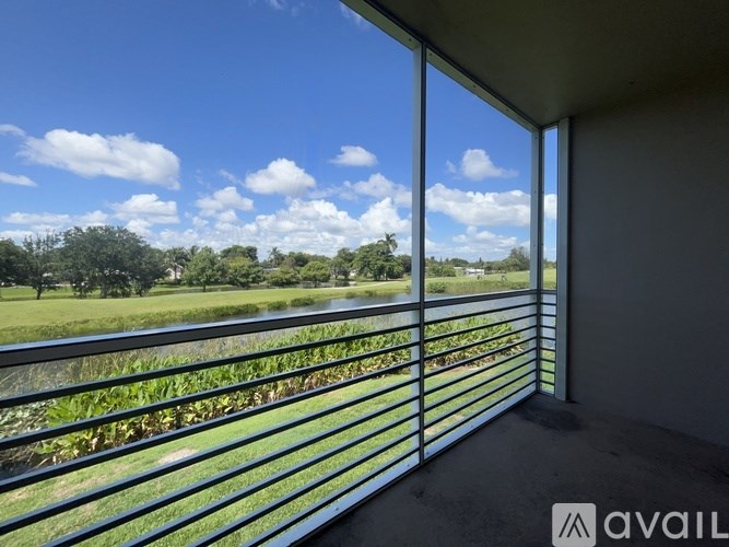 A balcony with a metal railing overlooking a field with a body of water and trees.