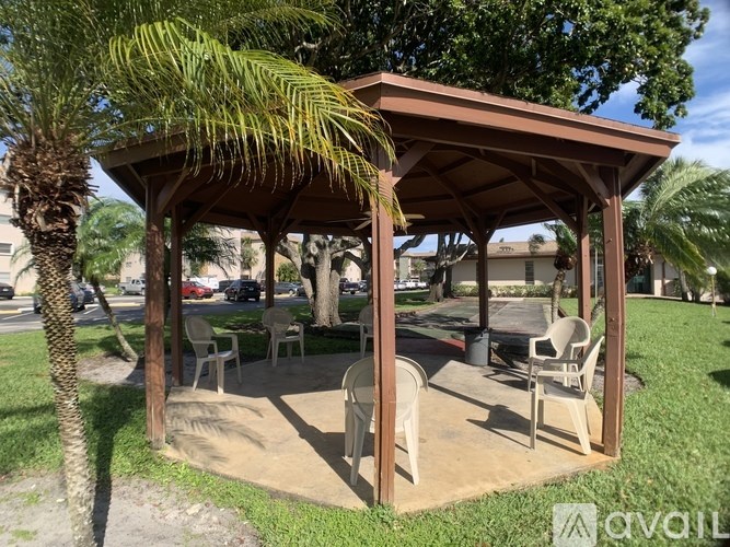A pavilion with chairs and a table is surrounded by trees.