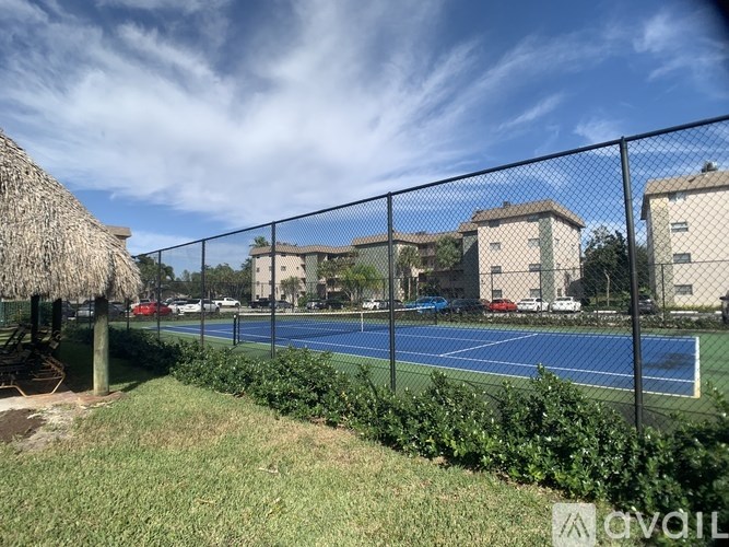 A tennis court is surrounded by a fence and there are buildings in the background.