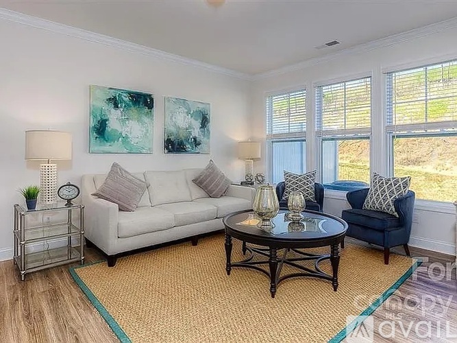 A living room with a white couch, a blue chair, and two abstract paintings on the wall.