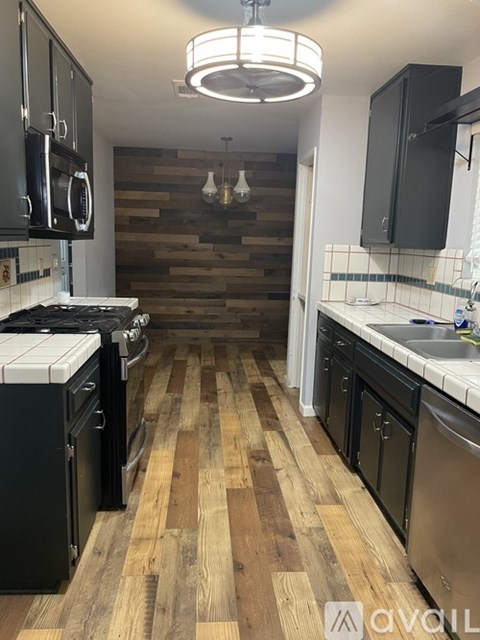 A kitchen with black appliances and wooden floors.