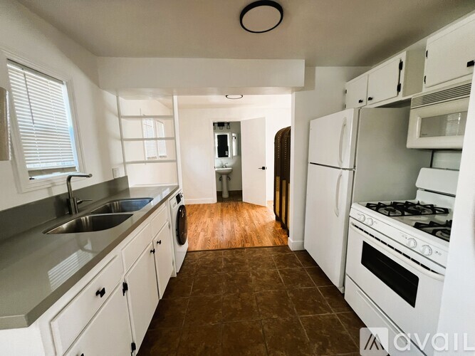 A kitchen with white appliances and brown flooring.