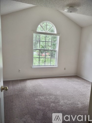 A room with a carpeted floor and a window with a view of trees and a fence.