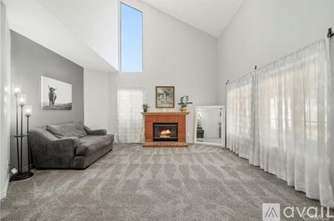 A living room with a grey couch, a fireplace, and a painting on the wall.