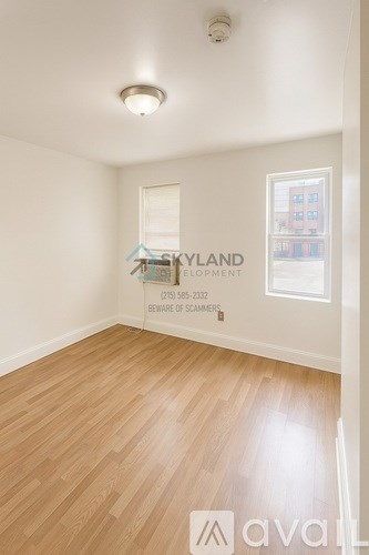 A room with wooden flooring and a window showing a building outside.