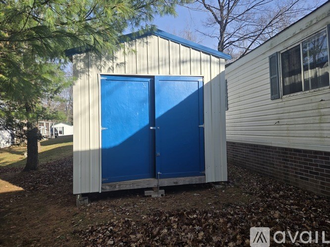 A blue and white storage shed sits in front of a house.