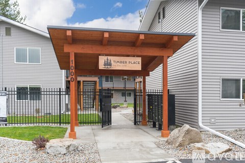 A timber place sign is on a wooden structure in front of a building.