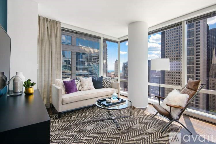 A living room with a white couch, a coffee table, and a chair with a view of the city.