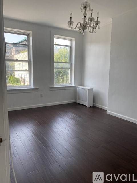 A room with a chandelier, two windows, and a wooden floor.