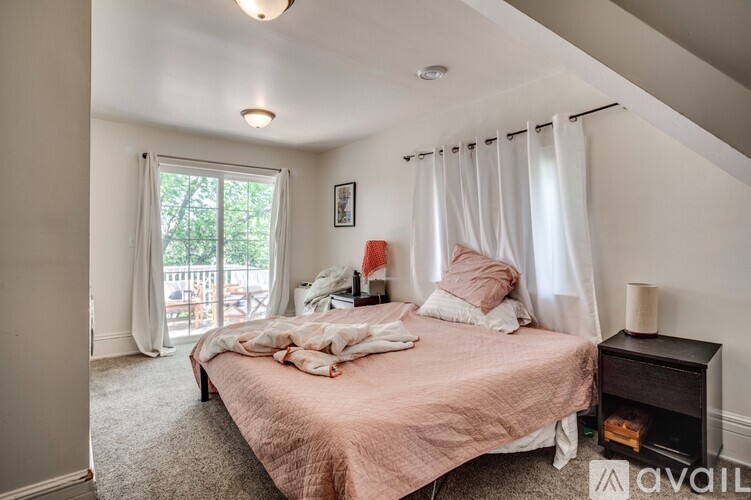 A bedroom with a bed, nightstand, and window with white curtains.