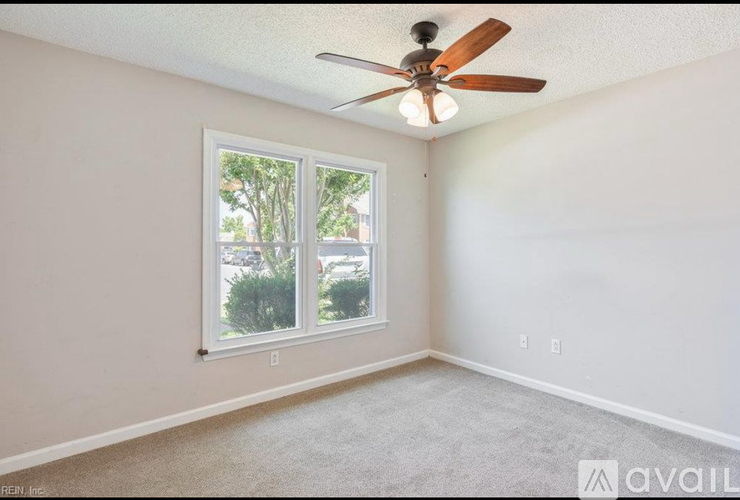 A room with a ceiling fan and a window overlooking a parking lot.