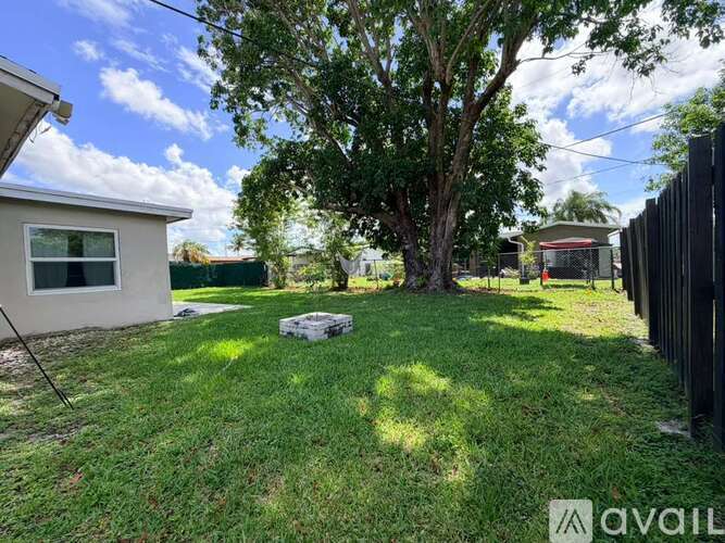 A tree in a yard with a house and fence in the background.