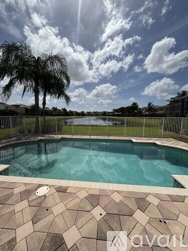 A swimming pool surrounded by a tiled floor and a fence with trees in the background.