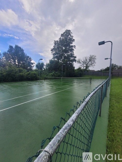 A tennis court with a green fence and trees in the background.