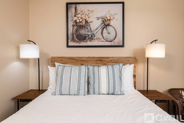 A bedroom with a bed, two lamps, and a framed picture of a bicycle.