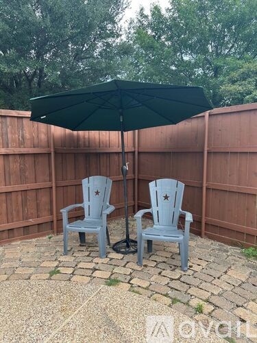 Two chairs are under a green umbrella in a backyard.