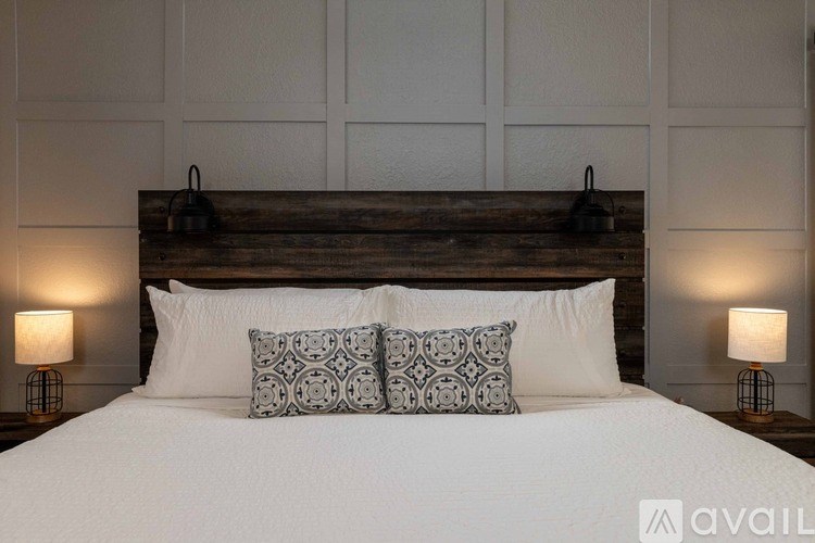 A bed with white bedding and two patterned pillows is flanked by two lamps on either side.