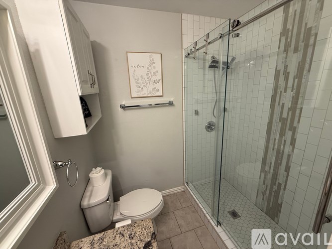 A bathroom with a toilet, a glass shower stall, and a picture on the wall.