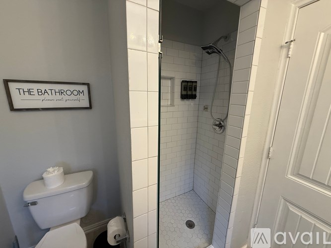 A bathroom with a toilet, a shower, and a sign on the wall.