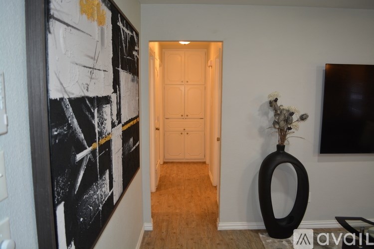 A hallway with a black and white painting on the wall and a vase with flowers on the floor.