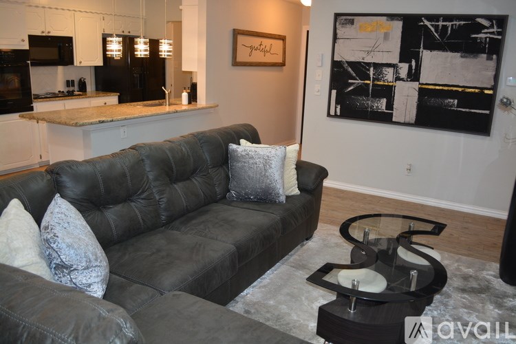 A black couch with a grey pillow is in the middle of a room with a black and white painting on the wall.