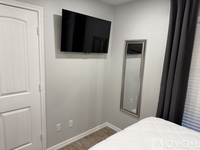 A bedroom with a bed, a door, a mirror, and a television mounted on the wall.