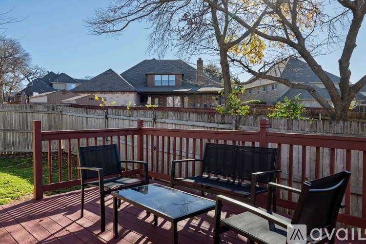 A wooden deck with a glass table and chairs overlooking a residential area.