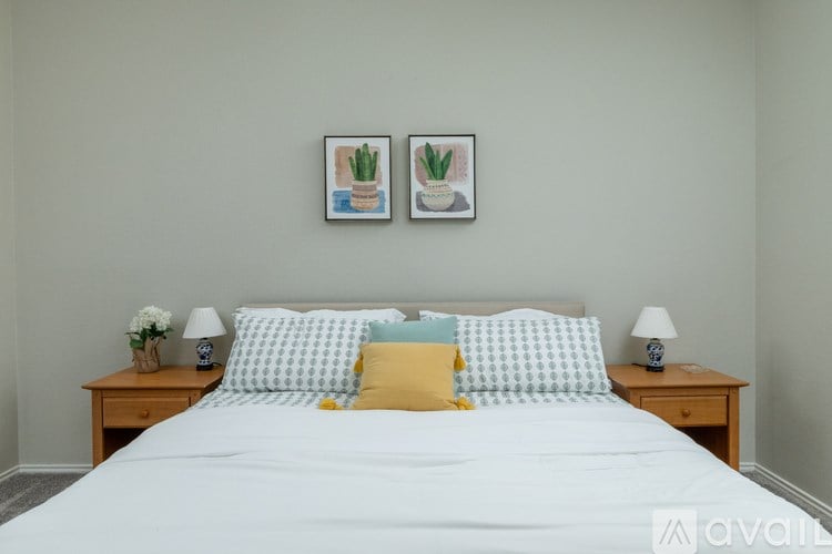 A bed with a white comforter and a yellow pillow is flanked by two small tables with lamps on them.