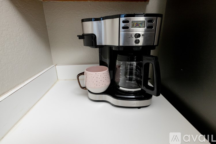 A coffee maker with a pink cup on a white surface.