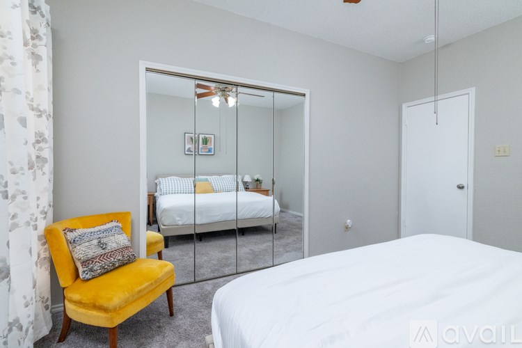 A bedroom with a white bed, a yellow chair, and a mirrored closet door.