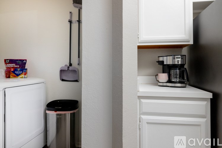 A small kitchen with a white fridge, a black trash can, and a white cabinet with a coffee maker on top.