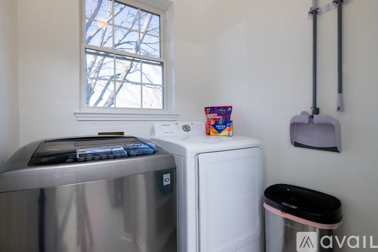 A room with a window, a washing machine, a trash bin, and a vacuum cleaner.