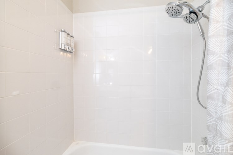 A white tiled shower with a shower head and a curtain.