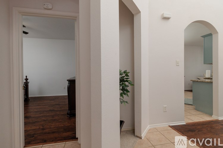 A room with a wooden floor and a white wall with a doorway leading to another room.