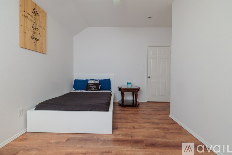 A bedroom with a bed, a small table, and a wooden sign on the wall.
