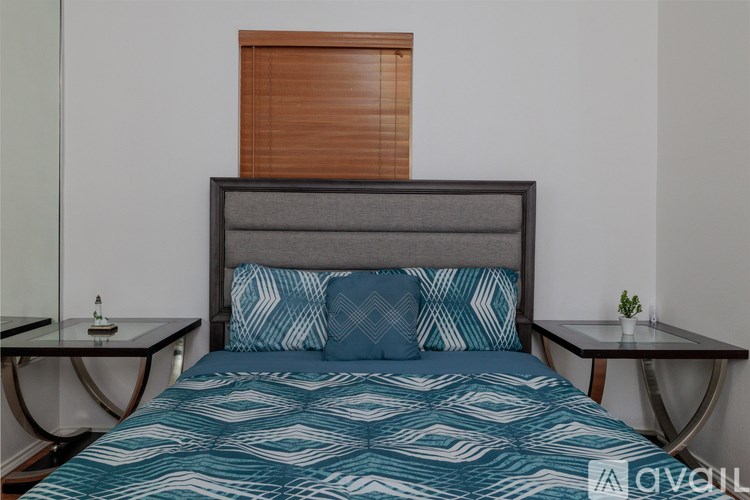 A bed with a blue and white patterned comforter and two matching pillows sits between two small tables.