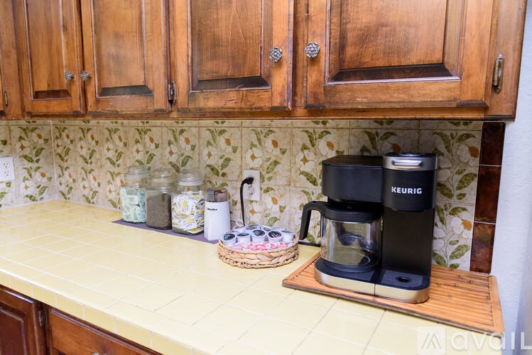 A Keurig coffee maker sits on a countertop with a basket of jars and containers.