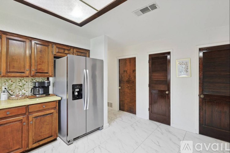 A kitchen with a refrigerator, wooden cabinets, and a marble floor.