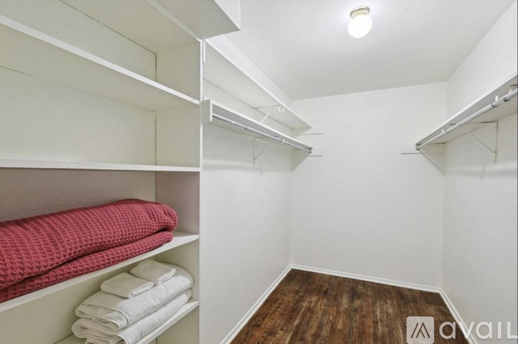 A small, white, and wood-floored room with a shelf and towels.