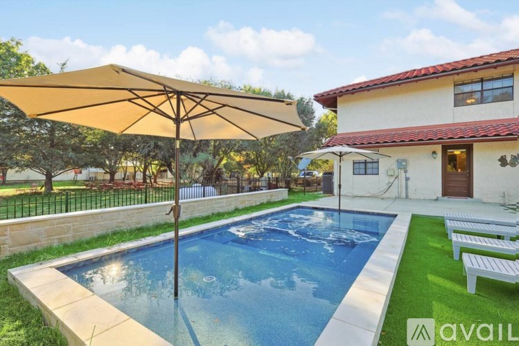 A pool with a sun umbrella in the foreground and a house in the background.