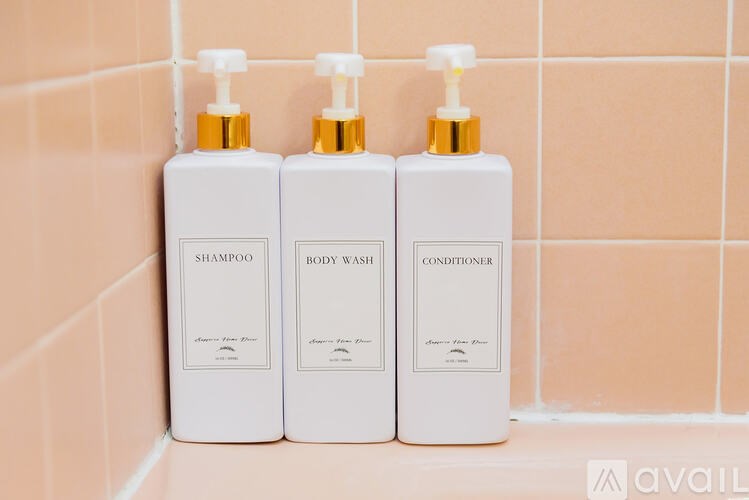 Three bottles of shampoo, body wash, and conditioner are lined up on a tiled wall.