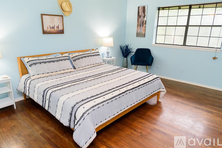 A bed with a striped comforter is in a room with wooden floors and a window.