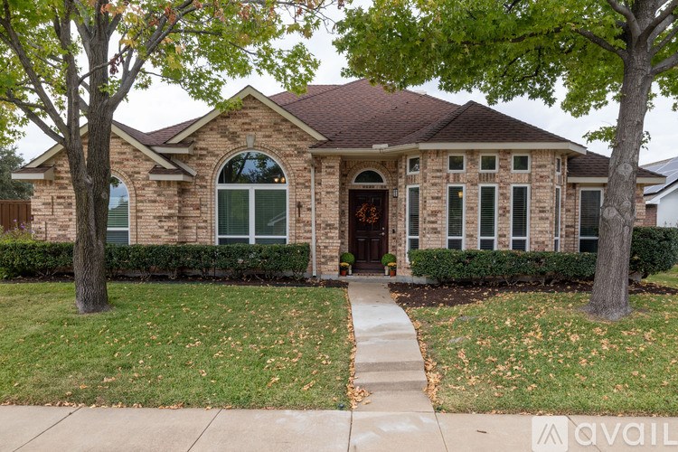A brick house with a brown roof and a front yard with a sidewalk.